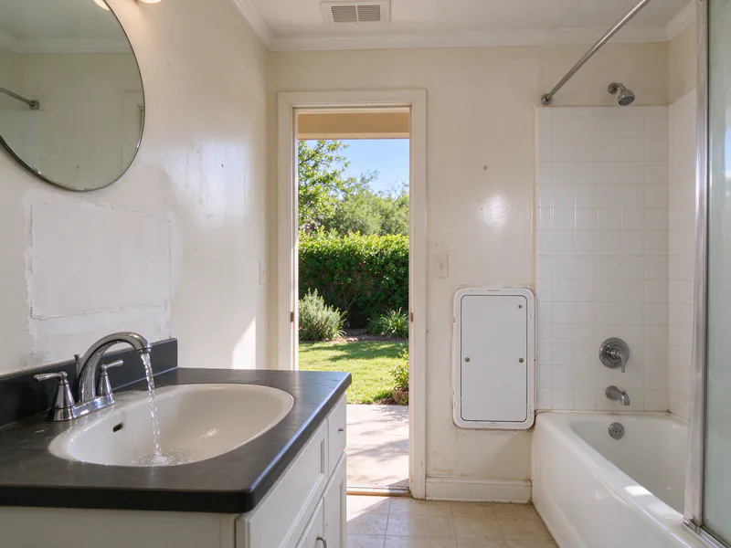 A patched wall and a new access panel in a hall bathroom of an Austin house after a partial repipe